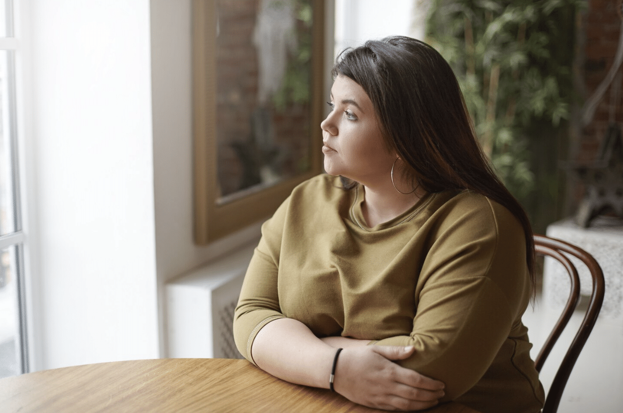 A plus-size woman sitting in a cafe feeling lonely and overwhelmed.