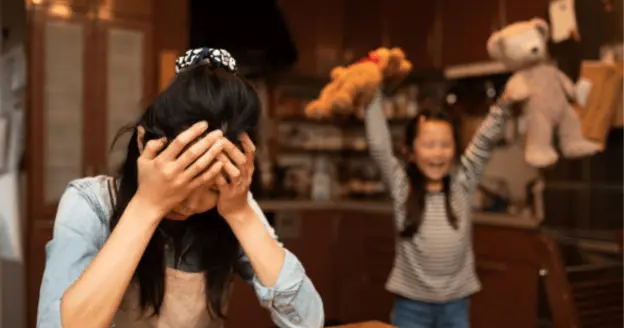 A woman holding her head with a young girl in the back 